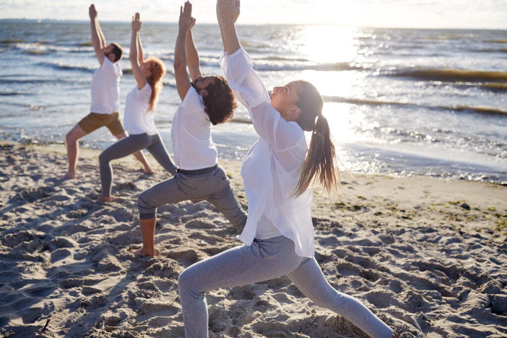 Group Of People Making Yoga Exercises On Beach