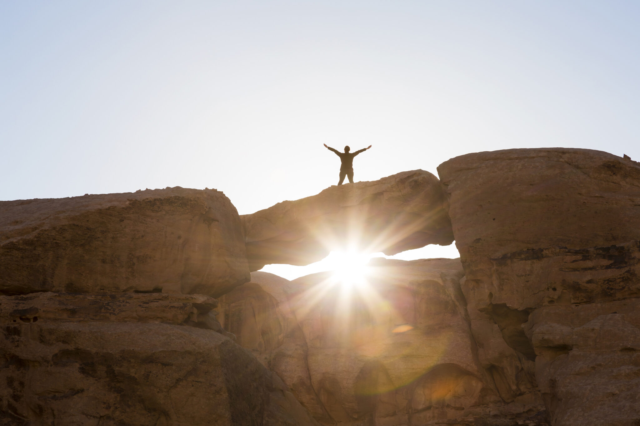 Wadi Rum,jordan,low Angle View Of Woman Standing With Her Arms Outstretched On A Natural Rock Bridge In The Desert.